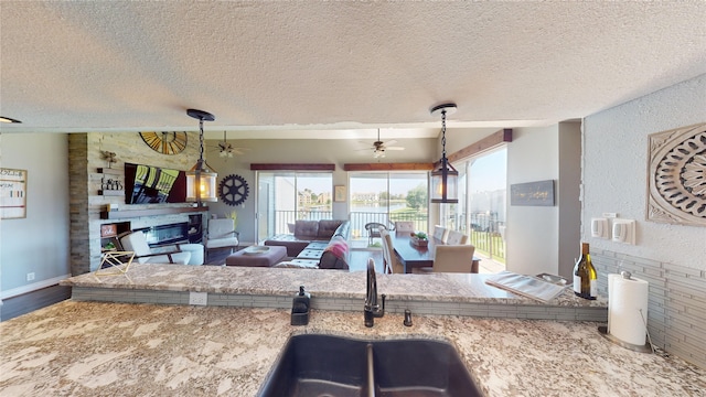 12500 Melville Dr Unit 211, Montgomery, TX 77356 - kitchen featuring a glass covered fireplace, a textured ceiling, a ceiling fan, open floor plan, and hanging light fixtures