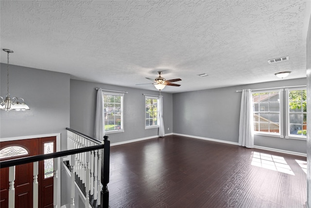 unfurnished room with ceiling fan with notable chandelier, a textured ceiling, visible vents, baseboards, and dark wood-style floors