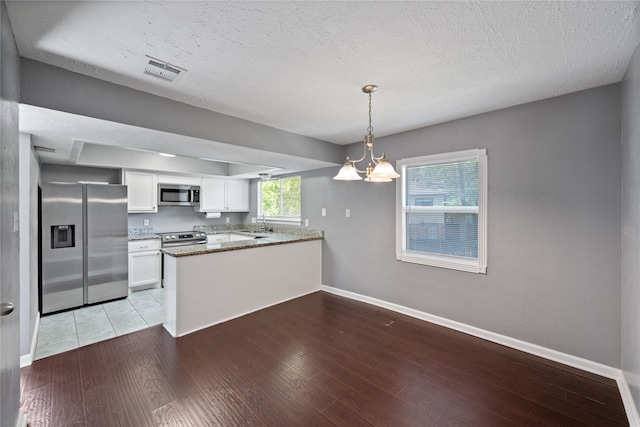 kitchen featuring a peninsula, white cabinets, visible vents, stainless steel appliances, and light wood finished floors