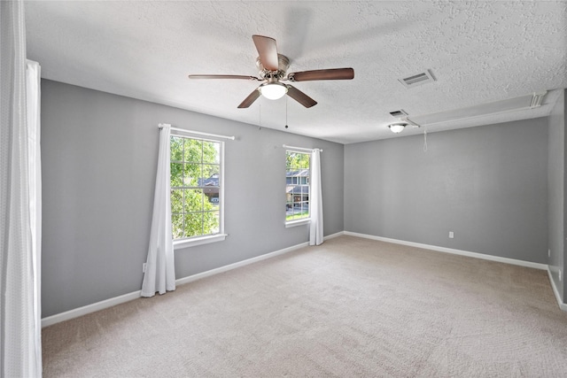 empty room with a textured ceiling, attic access, a ceiling fan, and carpet floors