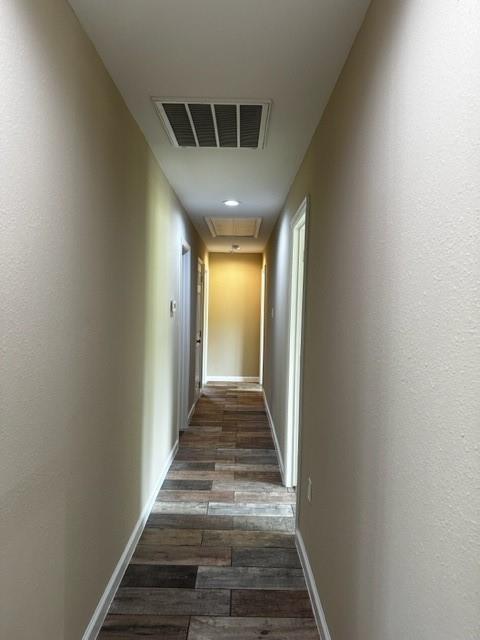 hall with visible vents, attic access, baseboards, and dark wood-style floors