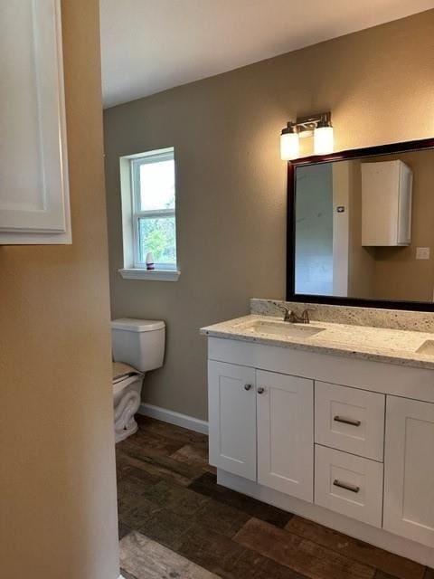 bathroom with double vanity, toilet, baseboards, and a sink