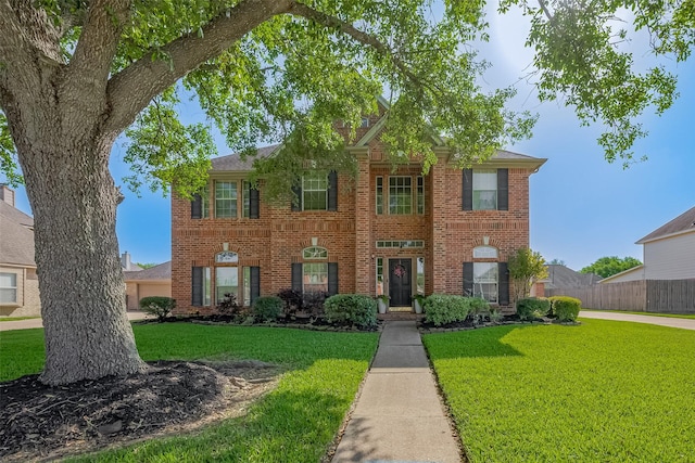 colonial home featuring brick siding, a front lawn, and fence