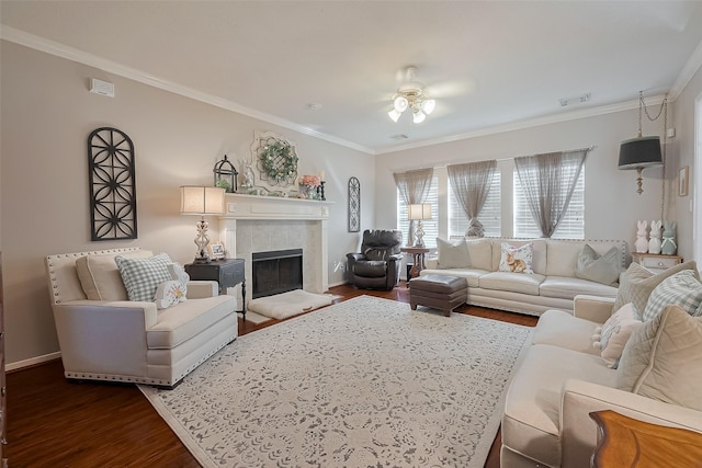living area featuring ceiling fan, dark wood finished floors, ornamental molding, a tile fireplace, and baseboards