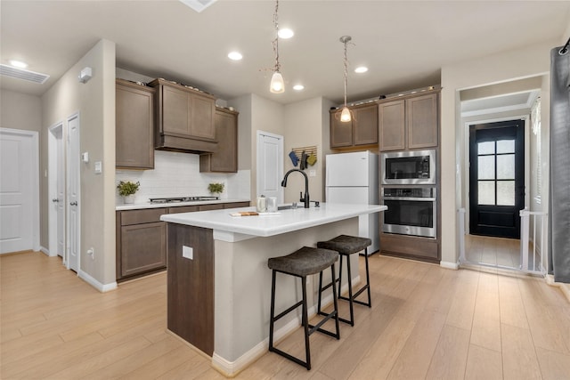 kitchen with a kitchen breakfast bar, light wood-style flooring, a sink, stainless steel appliances, and backsplash