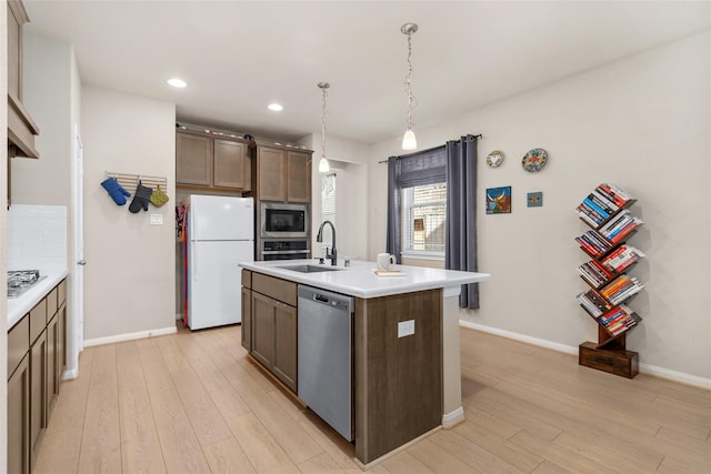 kitchen featuring baseboards, light countertops, stainless steel appliances, light wood finished floors, and a sink