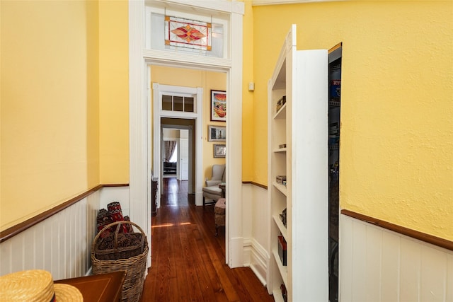 hallway with dark wood-type flooring, built in features, and wainscoting