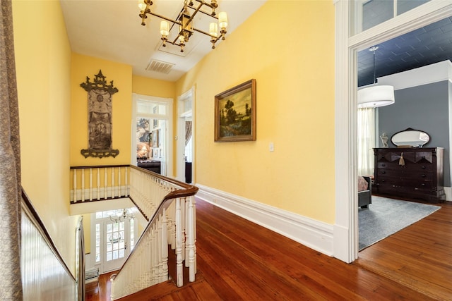 hallway featuring visible vents, baseboards, an inviting chandelier, an upstairs landing, and wood-type flooring