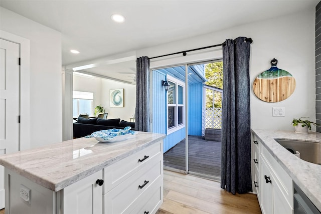 kitchen featuring light wood-type flooring, recessed lighting, white cabinetry, light stone countertops, and a sink