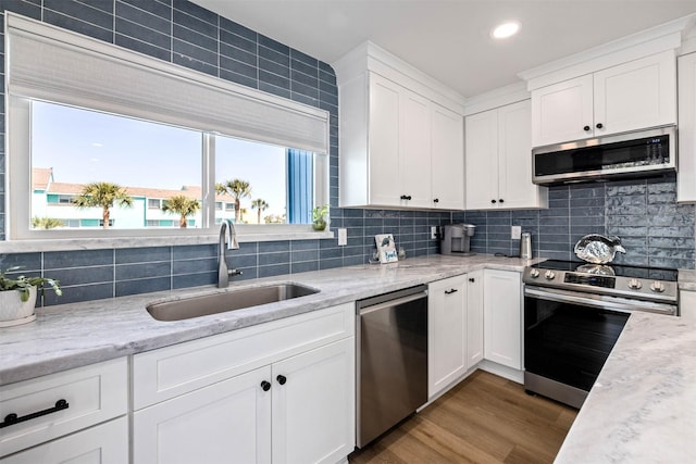 kitchen with backsplash, white cabinets, appliances with stainless steel finishes, a sink, and wood finished floors