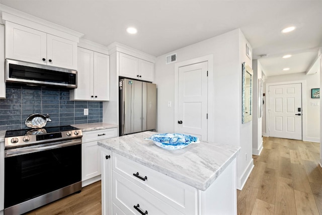kitchen with visible vents, light wood finished floors, stainless steel appliances, decorative backsplash, and light stone counters