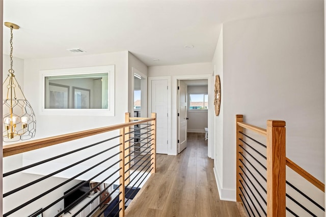 hall with an upstairs landing, visible vents, baseboards, and wood finished floors