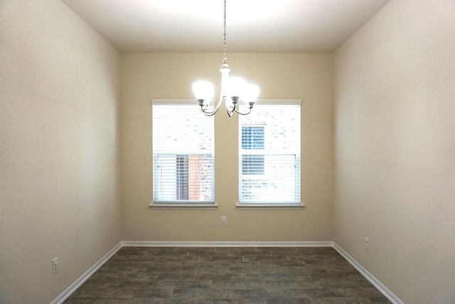 spare room with baseboards, an inviting chandelier, and dark wood finished floors