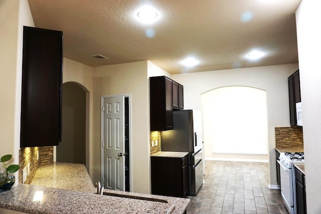 kitchen featuring visible vents, arched walkways, freestanding refrigerator, white range with gas cooktop, and decorative backsplash