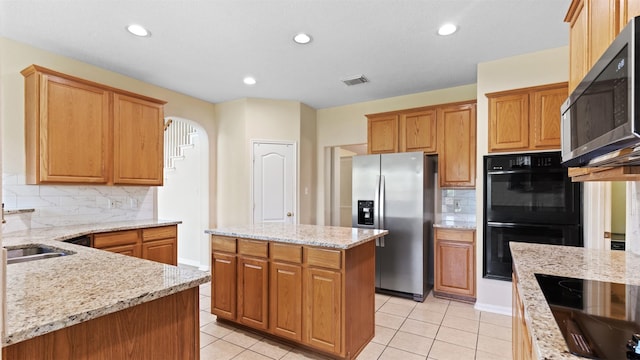 kitchen featuring light stone countertops, visible vents, backsplash, and black appliances