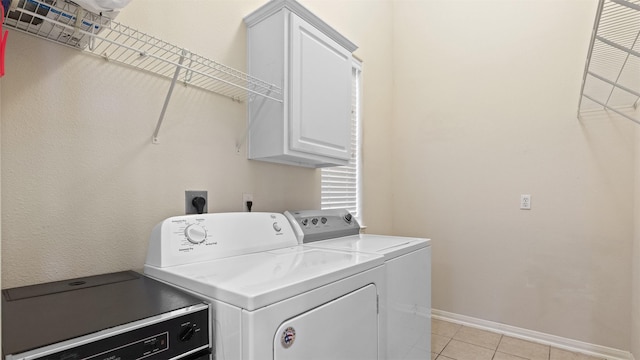 laundry area featuring washing machine and dryer, baseboards, cabinet space, and light tile patterned floors