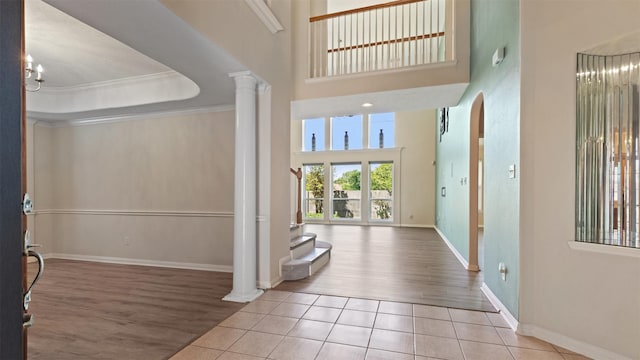 entryway with wood finished floors, a high ceiling, ornate columns, and crown molding