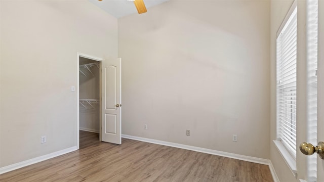 unfurnished bedroom with light wood-style flooring, a spacious closet, baseboards, and multiple windows