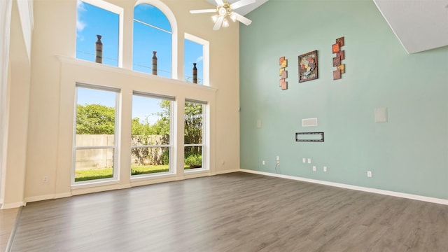 unfurnished living room featuring wood finished floors, a towering ceiling, baseboards, and ceiling fan