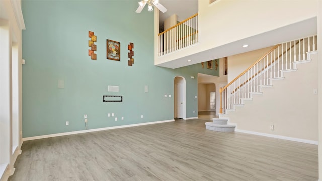 unfurnished living room featuring stairway, a high ceiling, wood finished floors, arched walkways, and ceiling fan