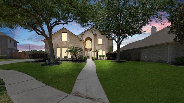 french country style house with fence, a lawn, and brick siding