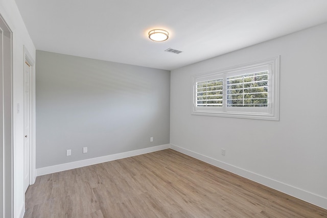 empty room featuring visible vents, light wood-type flooring, and baseboards