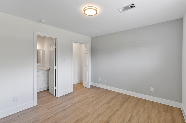 unfurnished bedroom featuring visible vents, baseboards, light wood-type flooring, and ensuite bath