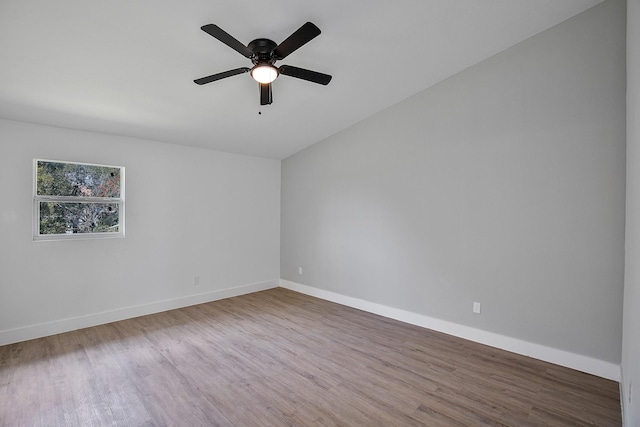 empty room featuring wood finished floors, ceiling fan, baseboards, and vaulted ceiling