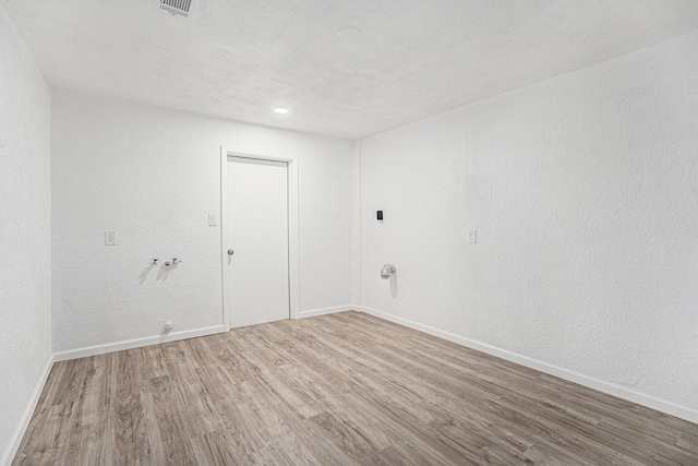 empty room with a textured ceiling, visible vents, wood finished floors, a textured wall, and baseboards