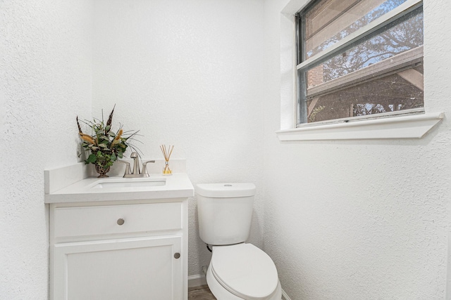 bathroom featuring toilet, vanity, and a textured wall