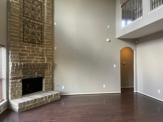 unfurnished living room featuring arched walkways, a towering ceiling, wood finished floors, and a fireplace