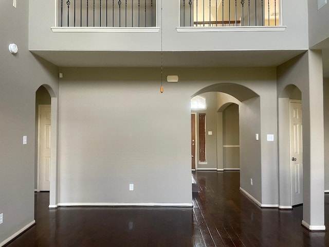 spare room with baseboards, a high ceiling, arched walkways, and wood finished floors
