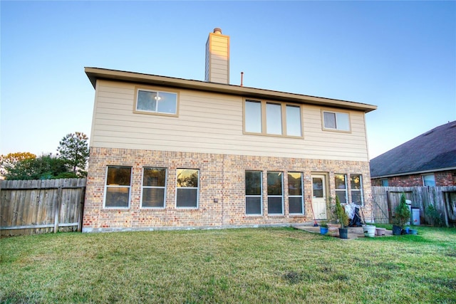 rear view of property with a lawn, a chimney, a fenced backyard, and brick siding