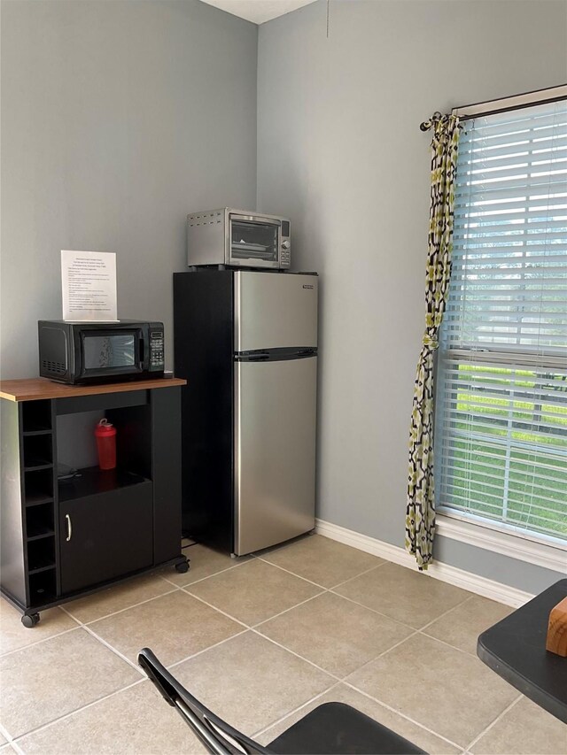 kitchen featuring freestanding refrigerator, baseboards, light tile patterned floors, and black microwave