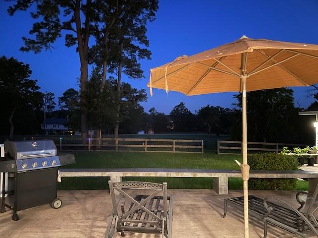 patio at twilight with a grill, a lawn, and fence