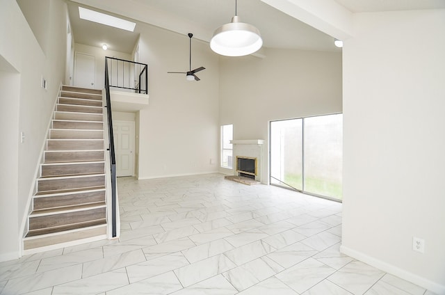 unfurnished living room featuring baseboards, a fireplace with raised hearth, stairs, ceiling fan, and high vaulted ceiling
