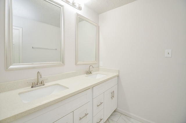 bathroom with double vanity, a textured ceiling, marble finish floor, and a sink
