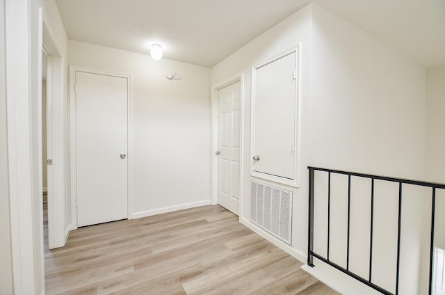 hall with visible vents, light wood finished floors, and baseboards