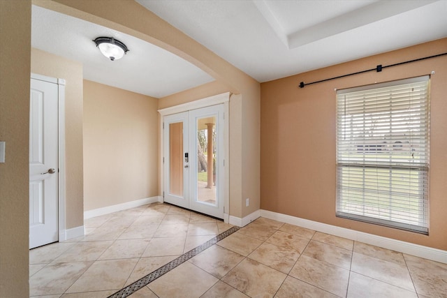 tiled entrance foyer featuring arched walkways, baseboards, and french doors