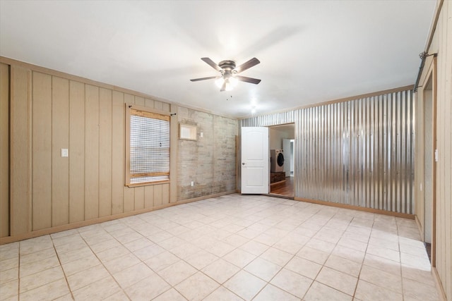 empty room featuring washer / dryer, a ceiling fan, wooden walls, and baseboards