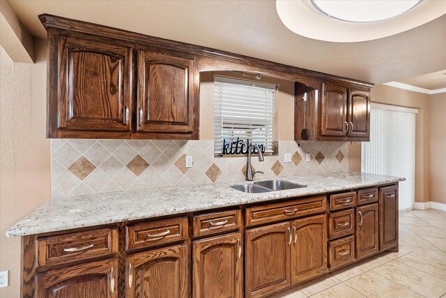 kitchen with light stone counters, tasteful backsplash, a sink, and light tile patterned floors