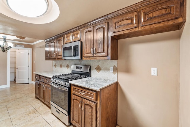 kitchen with baseboards, decorative backsplash, appliances with stainless steel finishes, light stone counters, and light tile patterned floors
