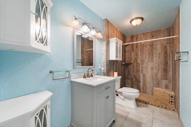 bathroom featuring toilet, a textured wall, tile patterned flooring, and a tile shower