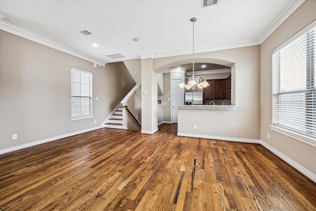 unfurnished living room with a chandelier, a healthy amount of sunlight, visible vents, ornamental molding, and dark wood-style floors