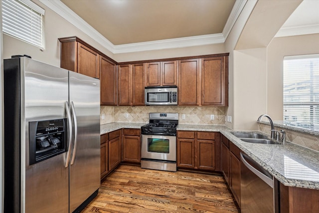 kitchen featuring a sink, wood finished floors, brown cabinets, light stone counters, and appliances with stainless steel finishes