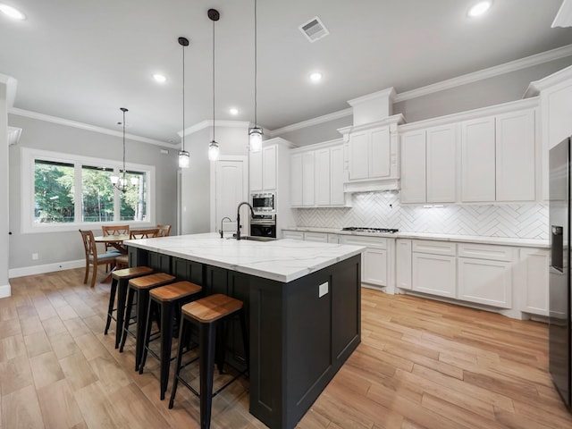 kitchen featuring white cabinets, an island with sink, stainless steel appliances, backsplash, and visible vents