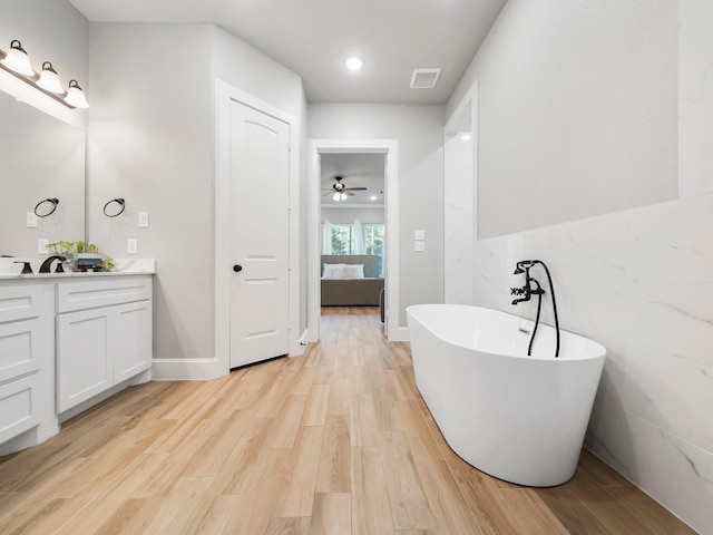 ensuite bathroom featuring a ceiling fan, wood finished floors, a freestanding tub, double vanity, and visible vents