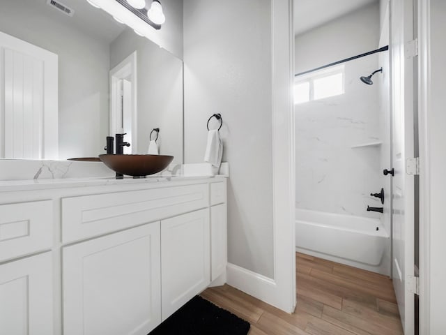 bathroom featuring wood finished floors, shower / bathing tub combination, vanity, baseboards, and visible vents