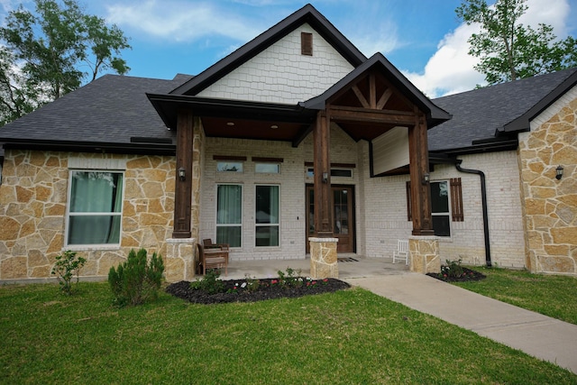 view of front of property with a shingled roof, a front lawn, covered porch, stone siding, and brick siding