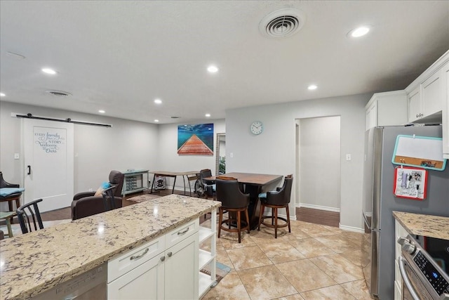 6360 Pansy Dr, Beaumont, TX 77706 - kitchen featuring light stone counters, white cabinets, a barn door, visible vents, and appliances with stainless steel finishes